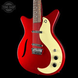 A red electric guitar with a cream-colored pickguard, shown against a solid black background. The brand logo on the headstock is not visible, and there is a Tone Shop watermark in the top-left corner.