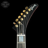 Close-up of a Gibson electric guitar headstock in black with gold tuning pegs and strings, shown against a black background with a Tone Shop watermark in the upper left.