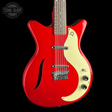 A red electric guitar with a cream-colored pickguard, shown against a solid black background. The Tone Shop logo is visible in the top-left corner.