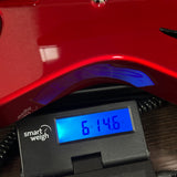 A close-up of a black smart weigh scale with a blue backlit display showing '614.6 kg' under a glossy red surface.