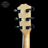 Close-up of the headstock of a six-string acoustic guitar, showing the natural wood grain and six black tuning pegs against a solid black background. A 'TONE SHOP' logo watermark is visible in the top left corner.