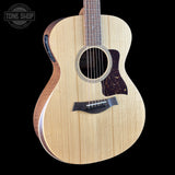 A close-up of an acoustic guitar body with a natural light wood finish, dark brown pickguard, and dark side binding, shown against a solid black background with a Tone Shop watermark in the top left.