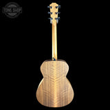 A close-up rear view of a wooden acoustic guitar against a solid black background, showing the back of the body and headstock. A Tone Shop watermark is visible in the top-left corner.