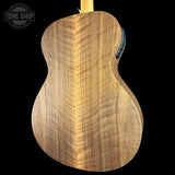 Close-up of the back of an acoustic guitar showing a beautiful figured wood grain pattern on a black background, with a Tone Shop watermark in the top left corner.