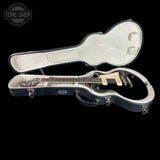 An electric guitar with a black body and cream pickguard displayed inside an open black hard guitar case with cream lining, set against a solid black background.