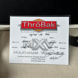 A ThróBak vintage reproduction parts card for a 1957-1959 SB Pro motorcycle, placed on a beige leather surface. The card features the ThróBak logo and handwritten details for wire lot, bridge, neck, and winders.