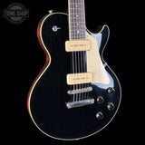 A black electric guitar with a glossy black finish, cream pickguard, and gold-toned hardware, shown against a solid black background. A Tone Shop logo is visible in the top-left corner.