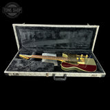 An electric guitar with a gold body, burgundy headstock, and gold hardware, displayed inside an open gray hard case with black velvet lining on a black background. A Tone Shop logo is visible in the top-left corner.