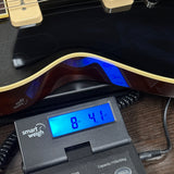 A close-up of a black electric guitar body resting on a digital smart weigh scale, showing the scale reading 8.41 kg.