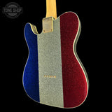 A close-up of the back of a double-cutaway electric guitar with a glittery French flag design: blue on the left, silver in the center, and red on the right, shown against a black background.