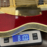 Close-up of a red glitter electric guitar body resting on a digital scale displaying 8.100 oz.