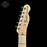 Close-up of a Fender Telecaster electric guitar headstock in natural maple wood, showing six silver tuning pegs and the black Fender Telecaster logo, set against a solid black background.