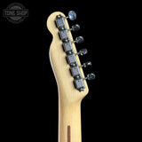 Close-up of the headstock of an electric guitar with a natural maple wood finish and six black tuning pegs, shown against a solid black background with a Tone Shop watermark in the top left corner.