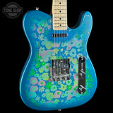 A blue electric guitar with a vibrant pink, green, and light blue floral pattern, shown against a solid black background with a Tone Shop watermark in the top-left corner.