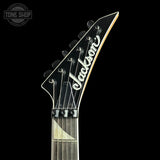 Close-up of the headstock of a Jackson electric guitar against a solid black background, showing the brand name 'Jackson' in white script on a glossy black headstock.