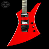 A bright red electric guitar with a distinctive angular body, black hardware, and a dark fretboard, shown against a solid black background. A Tone Shop watermark is visible in the top-left corner.