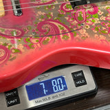 A close-up of a pink electric guitar body with a floral and paisley pattern, resting on a digital scale displaying 7.80 oz.