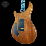 A close-up of an electric guitar's body, showing a warm brown wood grain finish with black pickguard plates and a blue marbled neck, set against a solid black background.