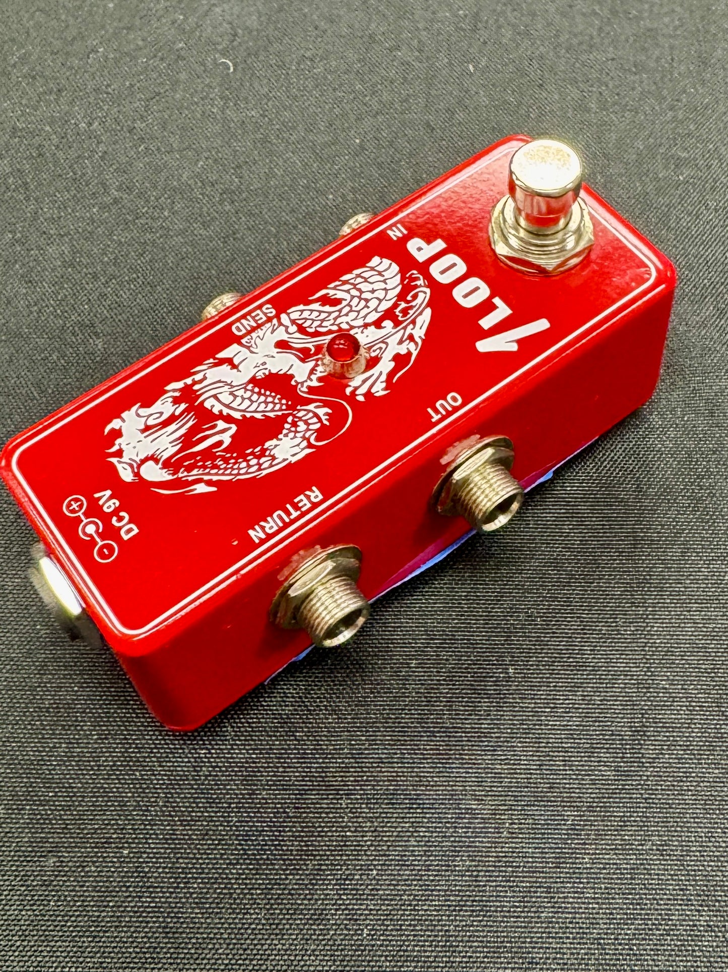 Red guitar effects pedal with dragon design on a gray background