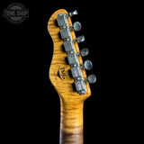 Close-up of the headstock of a TME electric guitar, showing the maple wood backplate with a natural flame maple pattern, six silver tuning pegs, and the TME logo, set against a solid black background.
