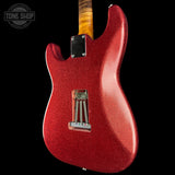 A close-up of a red glitter electric guitar body, showing the back side with a black pickup cover, silver hardware, and part of a yellow wood neck against a black background. A Tone Shop watermark is visible in the top left corner.