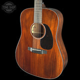 A close-up studio shot of a wooden acoustic guitar body against a black background, showing the rich brown wood grain, circular soundhole, pickguard, and bridge. A Tone Shop logo watermark is visible in the top-left corner.