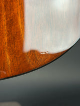Close-up of a curved wooden surface with a glossy finish, showing warm brown wood grain and a light reflection, against a dark gray background.