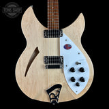 A double-cutaway electric guitar with a natural wood body, white pickguard, and black hardware, shown against a solid black background. A Tone Shop watermark is visible in the top left corner.