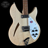 A double-cutaway electric bass guitar with a natural wood finish body, white pickguard, and black hardware, shown against a solid black background. A Tone Shop watermark is visible in the top left corner.