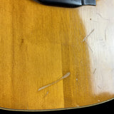 Close-up of a wooden guitar with a visible grain pattern on a light wood surface.