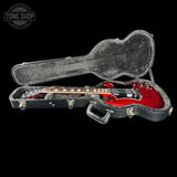 A red electric guitar inside an open black hard case on a black background, with a Tone Shop watermark in the top left corner.