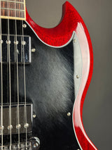 Close-up of an electric guitar body showing a glossy red maple edge, black pickguard, chrome hardware, and part of the fretboard against a dark gray background.