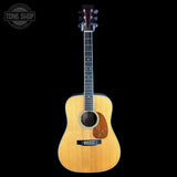 A natural wood acoustic guitar with a dark headstock, shown vertically against a solid black background. A circular 'TONE SHOP' watermark is visible in the top-left corner.