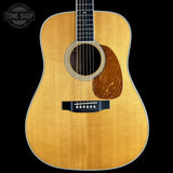 A front-facing acoustic guitar with a natural wood finish and dark fretboard, shown against a solid black background with a Tone Shop watermark in the top-left corner.