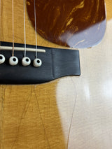Close-up of an acoustic guitar's bridge, showing the black wood bridge plate, white tuning pegs, strings, and part of the brown marbled soundboard on a light wood body.