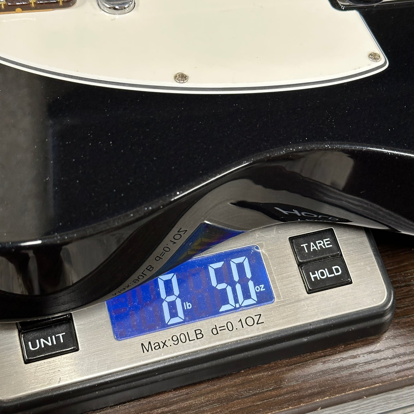 Digital scale displaying weight of a black object on a wooden surface
