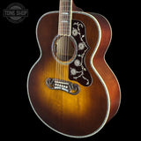 A close-up of an acoustic guitar body with a natural sunburst finish, featuring a decorative floral pickguard and a Tone Shop logo watermark in the top left corner.
