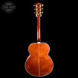 The back of an acoustic guitar with a glossy reddish-brown wood finish, featuring gold tuning pegs and a white edge stripe, shown against a solid black background with a Tone Shop watermark in the top left corner.