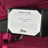 A Gibson Custom Certificate of Authenticity card displayed inside a black presentation box, resting on a deep burgundy velvet fabric background.