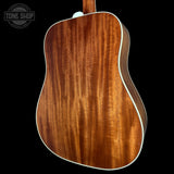 Close-up of the back of an acoustic guitar showing a rich, warm brown wood grain finish with a white edge trim, set against a solid black background.