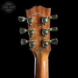 Close-up of the headstock of a wooden acoustic guitar, showing six tuning pegs, serial number 21396024, 'MADE IN USA' on a black background with a Tone Shop watermark.