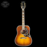 A vintage-style acoustic guitar with a sunburst finish, featuring floral inlay on the pickguard and headstock, shown against a solid black background with a Tone Shop watermark in the top left corner.