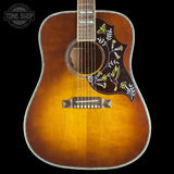 A close-up of an acoustic guitar body showing a natural sunburst finish that fades to black around the edges, with a dark brown pickguard decorated with yellow birds and white floral patterns. The brand 'TONE SHOP' is visible as an overlay in the top left corner.