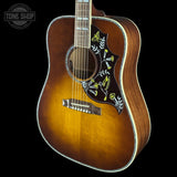 A vintage acoustic guitar with a natural sunburst finish, featuring a black pickguard decorated with yellow and white bird and floral motifs. The guitar is shown against a solid black background with a Tone Shop watermark in the top left corner.