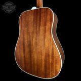 The back of an acoustic guitar with a rich, warm brown wood grain finish and white binding, shown against a solid black background with a Tone Shop watermark in the top left.