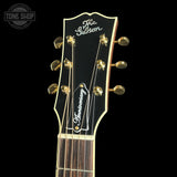 Close-up of the headstock of a Gibson electric guitar, featuring a black headstock with gold tuning pegs, white Gibson and Anniversary script logos, and a dark wood fretboard against a black background.