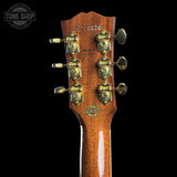 Close-up of the headstock of a Fender Stratocaster electric guitar, showing the six gold-toned tuning pegs, serial number 20716026, and a glossy brown wood finish against a black background.