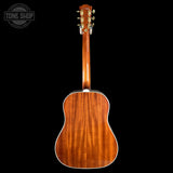The back of an acoustic guitar with a rich reddish-brown wood finish and gold tuning keys, shown against a solid black background with a Tone Shop watermark in the top-left corner.