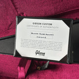 A close-up of a Gibson Custom Certificate of Authenticity card inside a black sleeve, placed on a deep magenta satin fabric background.