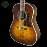 A close-up of an acoustic guitar body showing a natural wood sunburst finish that fades from bright amber-orange in the center to darker brown at the edges, with a black pickguard and white binding, set against a solid black background.